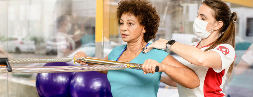 senhora fazendo exercicio em uma maquina com auxílio de um profissional